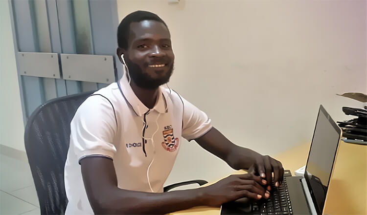 A smiling Mr. Bitanyanmi sits at his laptop.