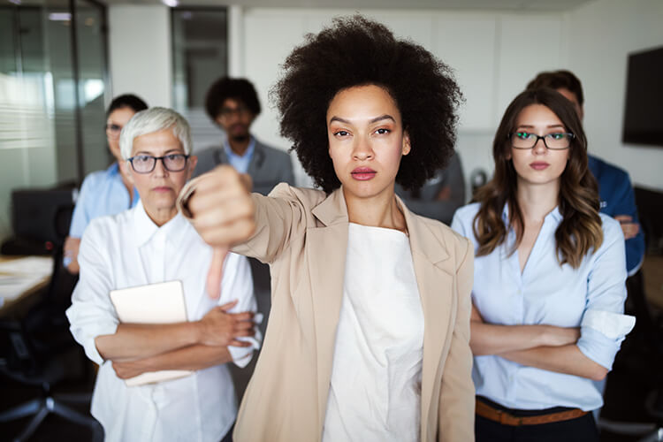 photograph of woman standing in front of colleagues, giving thumbs down