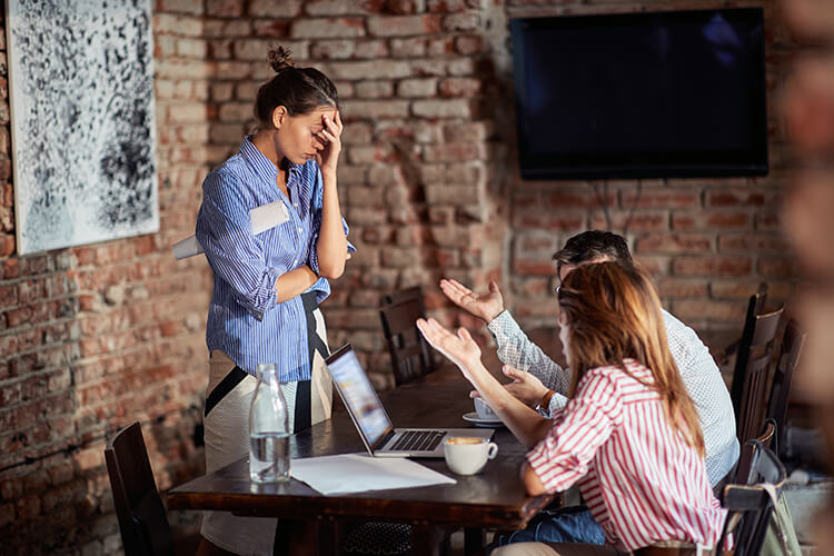 man and woman in a meeting gesture impatiently and expectantly at another woman who appears to be frazzled or stressed