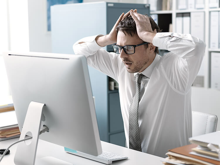 An office worker reacts with horror at something he sees on his computer screen.